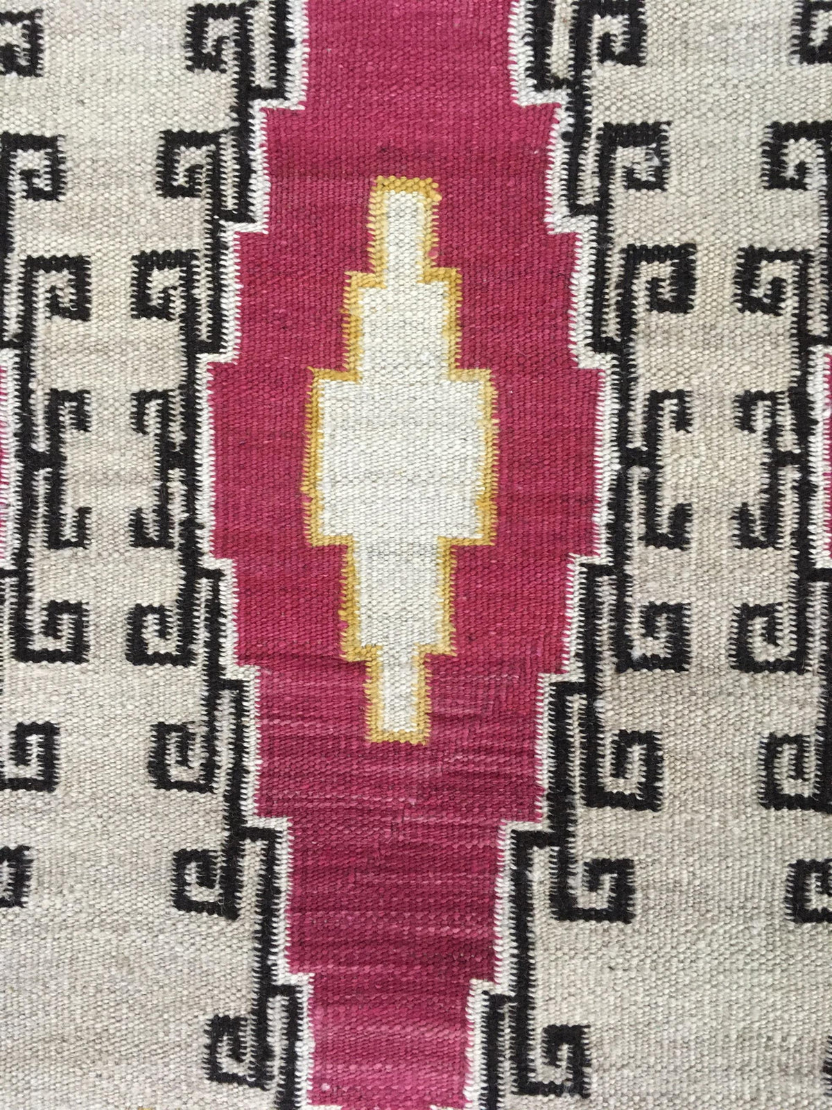 Close-up of a woven textile pattern with a central vertical magenta-pink stripe, a cream diamond motif outlined in yellow, and black geometric border patterns on a light beige background.Atlantica Organics curates antique and handmade rugs, Persian, Afghan, Tibetan, Pakistani, Turkish Oushak, Kilim, Khotan, tribal and contemporary textiles for luxury interiors, homes and real estate. Our collections connect timeless craftsmanship with interior design, furniture, fine art, architecture and modern living. Exp