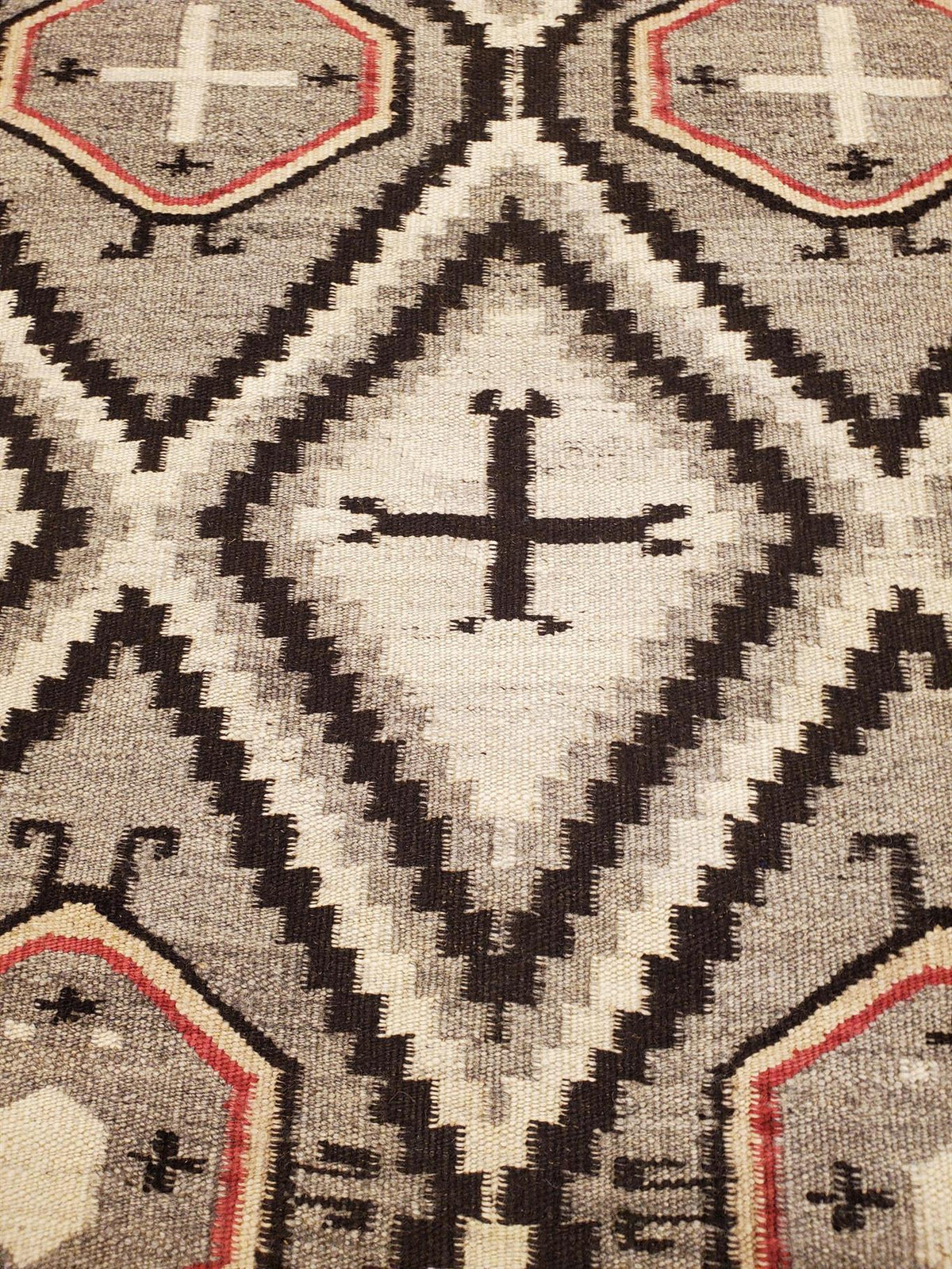 Close-up of a woven textile with a geometric Southwestern-style pattern in gray, black, off-white, and red.Atlantica Organics curates antique and handmade rugs, Persian, Afghan, Tibetan, Pakistani, Turkish Oushak, Kilim, Khotan, tribal and contemporary textiles for luxury interiors, homes and real estate. Our collections connect timeless craftsmanship with interior design, furniture, fine art, architecture and modern living. Explore curated rugs, collectible textiles, natural materials, cultural heritage, s
