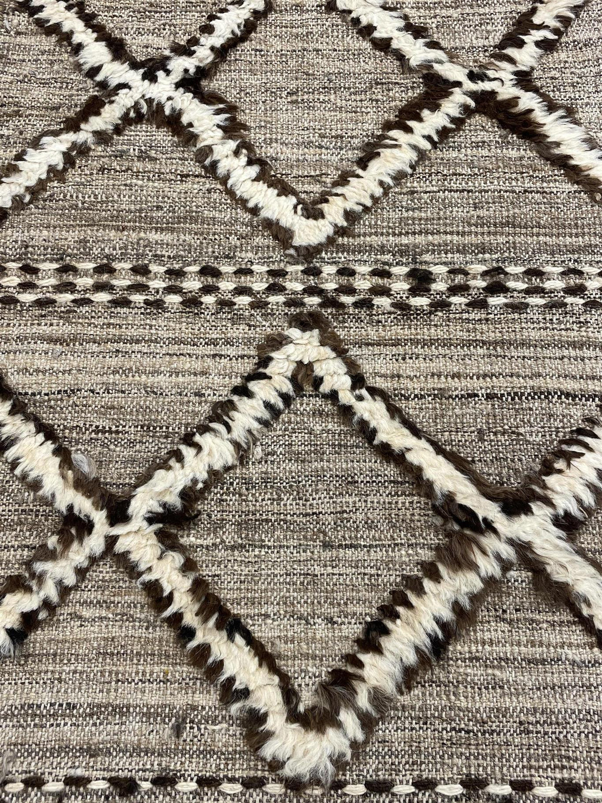 Close-up of a woven textile with a geometric diamond pattern in cream, brown, and beige.Atlantica Organics curates antique and handmade rugs, Persian, Afghan, Tibetan, Pakistani, Turkish Oushak, Kilim, Khotan, tribal and contemporary textiles for luxury interiors, homes and real estate. Our collections connect timeless craftsmanship with interior design, furniture, fine art, architecture and modern living. Explore curated rugs, collectible textiles, natural materials, cultural heritage, sustainable design a