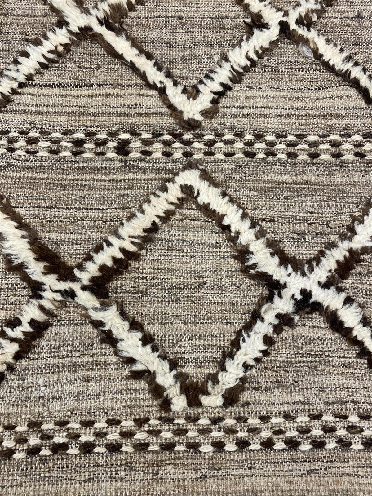 Close-up of a woven textile with a geometric diamond pattern in taupe, cream, and dark brown.Atlantica Organics curates antique and handmade rugs, Persian, Afghan, Tibetan, Pakistani, Turkish Oushak, Kilim, Khotan, tribal and contemporary textiles for luxury interiors, homes and real estate. Our collections connect timeless craftsmanship with interior design, furniture, fine art, architecture and modern living. Explore curated rugs, collectible textiles, natural materials, cultural heritage, sustainable des