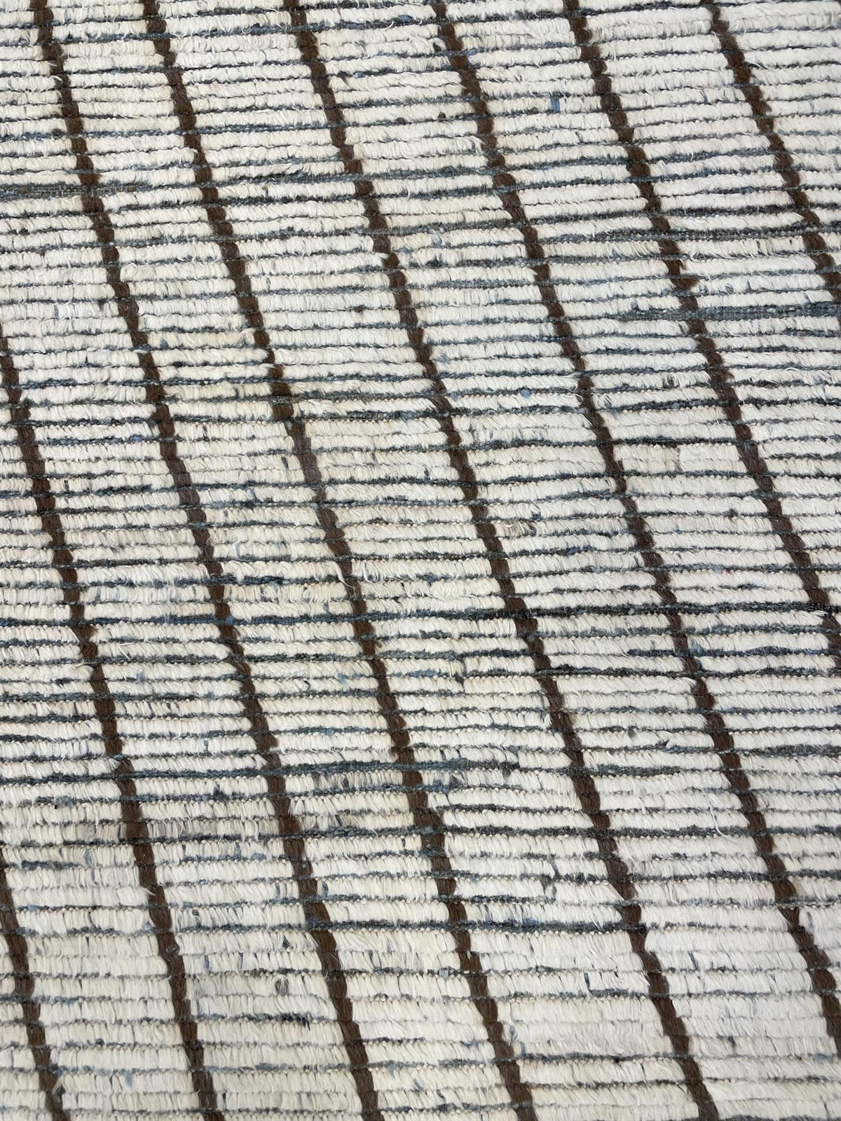 A close-up of a textured woven fabric with a cream base and dark brown vertical stripes. Atlantica Organics curates antique and handmade rugs, Persian, Afghan, Tibetan, Pakistani, Turkish Oushak, Kilim, Khotan, tribal and contemporary textiles for luxury interiors, homes and real estate. Our collections connect timeless craftsmanship with interior design, furniture, fine art, architecture and modern living. Explore curated rugs, collectible textiles, natural materials, cultural heritage, sustainable design 