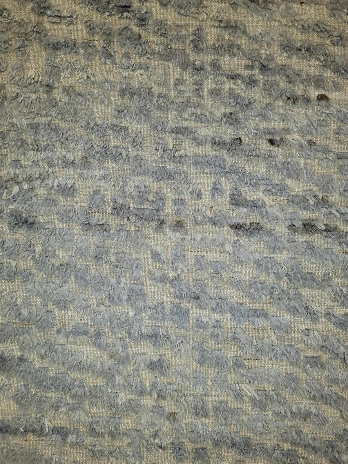 A close-up of a textured woven fabric with a mottled pattern of gray and beige threads. Atlantica Organics curates antique and handmade rugs, Persian, Afghan, Tibetan, Pakistani, Turkish Oushak, Kilim, Khotan, tribal and contemporary textiles for luxury interiors, homes and real estate. Our collections connect timeless craftsmanship with interior design, furniture, fine art, architecture and modern living. Explore curated rugs, collectible textiles, natural materials, cultural heritage, sustainable design a