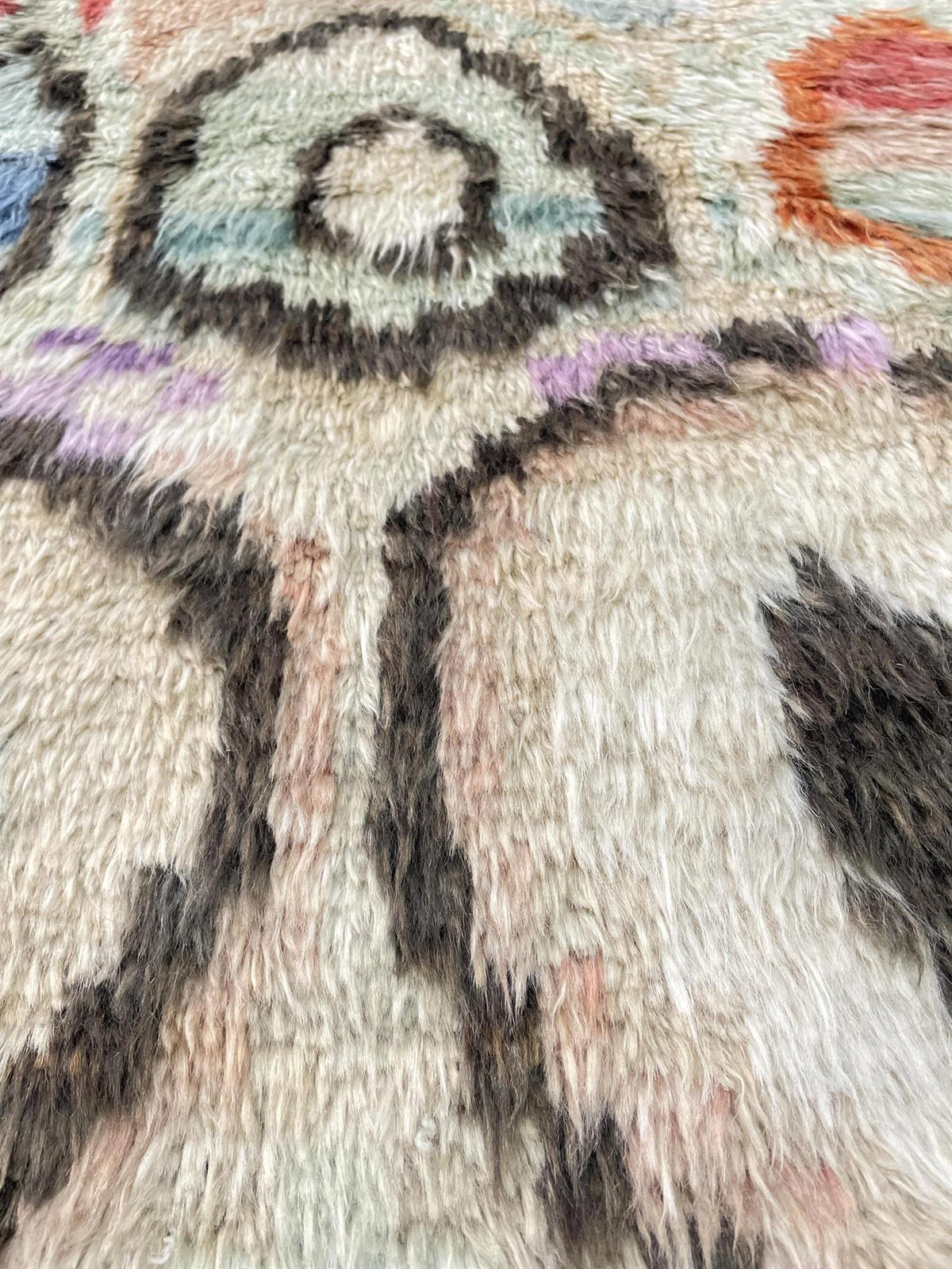 Close-up of a shaggy textured rug with abstract painted motifs in cream, black, purple, orange, and light blue.Atlantica Organics curates antique and handmade rugs, Persian, Afghan, Tibetan, Pakistani, Turkish Oushak, Kilim, Khotan, tribal and contemporary textiles for luxury interiors, homes and real estate. Our collections connect timeless craftsmanship with interior design, furniture, fine art, architecture and modern living. Explore curated rugs, collectible textiles, natural materials, cultural heritag