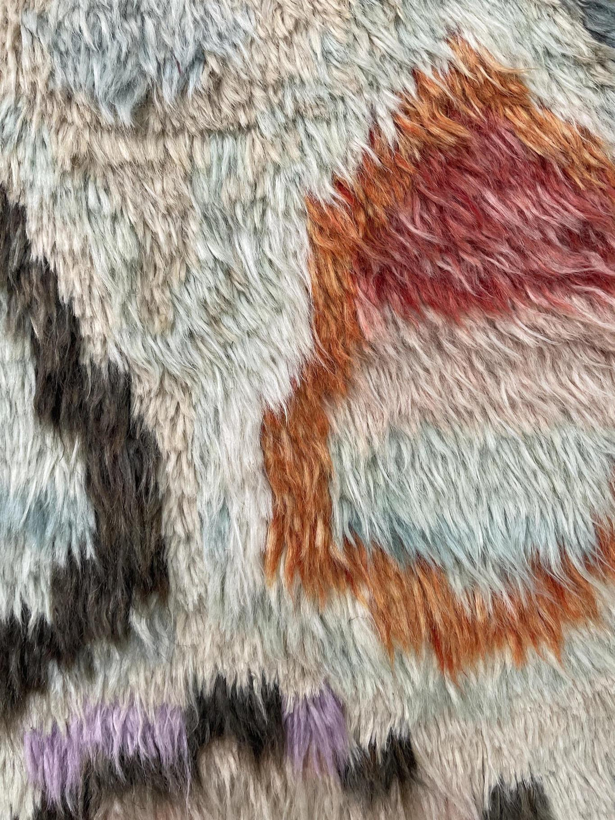 Close-up of a shaggy, textured rug or fabric with an abstract pattern in light gray, rust orange, dusty red, black, and small purple accents.Atlantica Organics curates antique and handmade rugs, Persian, Afghan, Tibetan, Pakistani, Turkish Oushak, Kilim, Khotan, tribal and contemporary textiles for luxury interiors, homes and real estate. Our collections connect timeless craftsmanship with interior design, furniture, fine art, architecture and modern living. Explore curated rugs, collectible textiles, natur