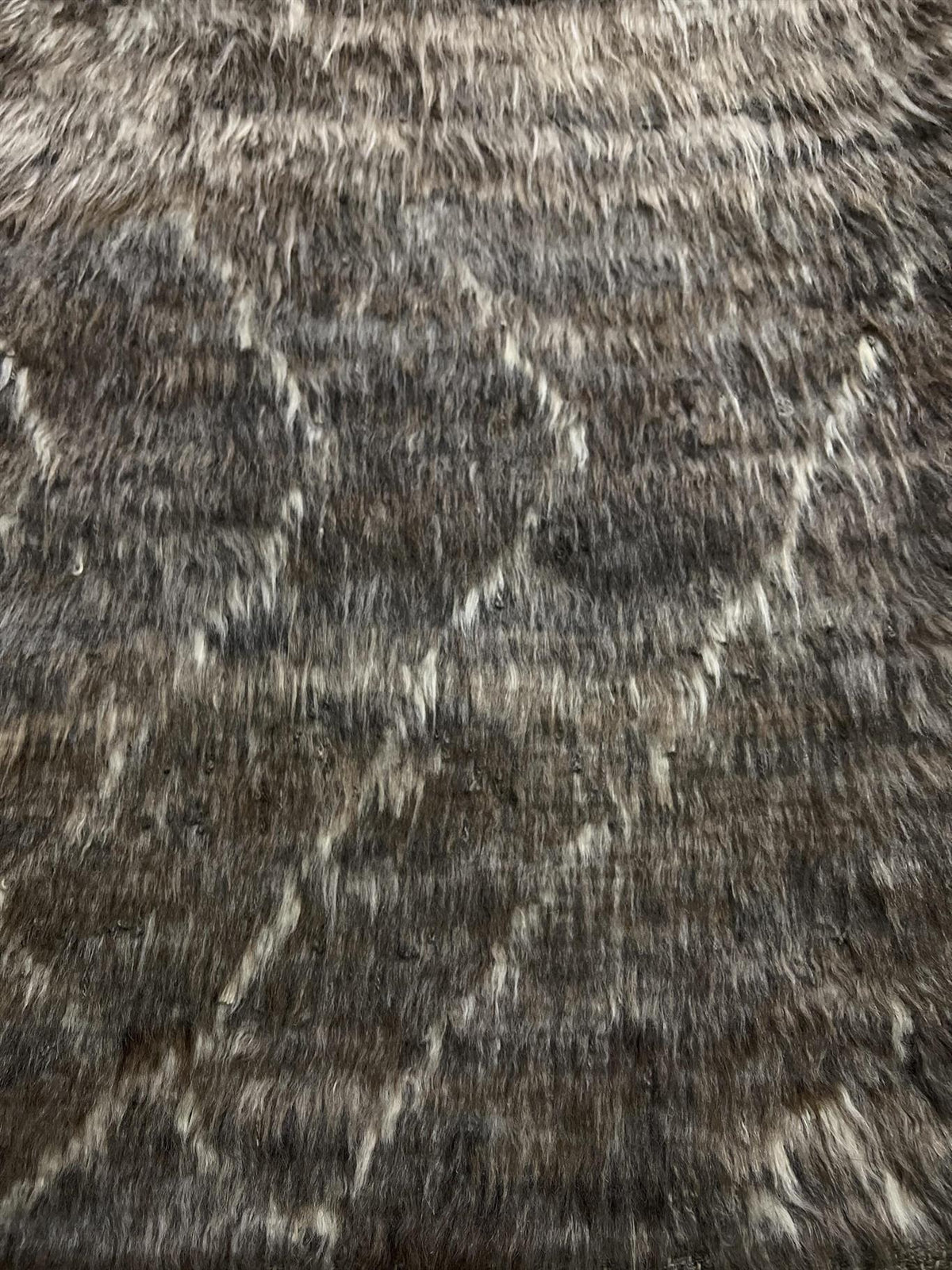 A close-up of a textured faux fur or shag rug with a dark brown and black base and light beige geometric line patterns. Atlantica Organics curates antique and handmade rugs, Persian, Afghan, Tibetan, Pakistani, Turkish Oushak, Kilim, Khotan, tribal and contemporary textiles for luxury interiors, homes and real estate. Our collections connect timeless craftsmanship with interior design, furniture, fine art, architecture and modern living. Explore curated rugs, collectible textiles, natural materials, cultura