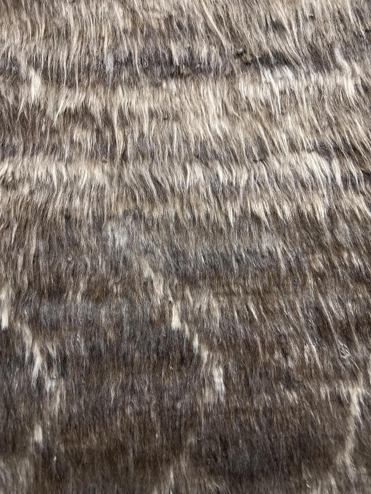 A close-up texture shot of a shaggy faux fur or animal-print fabric in mottled brown, gray, and cream tones. Atlantica Organics curates antique and handmade rugs, Persian, Afghan, Tibetan, Pakistani, Turkish Oushak, Kilim, Khotan, tribal and contemporary textiles for luxury interiors, homes and real estate. Our collections connect timeless craftsmanship with interior design, furniture, fine art, architecture and modern living. Explore curated rugs, collectible textiles, natural materials, cultural heritage,