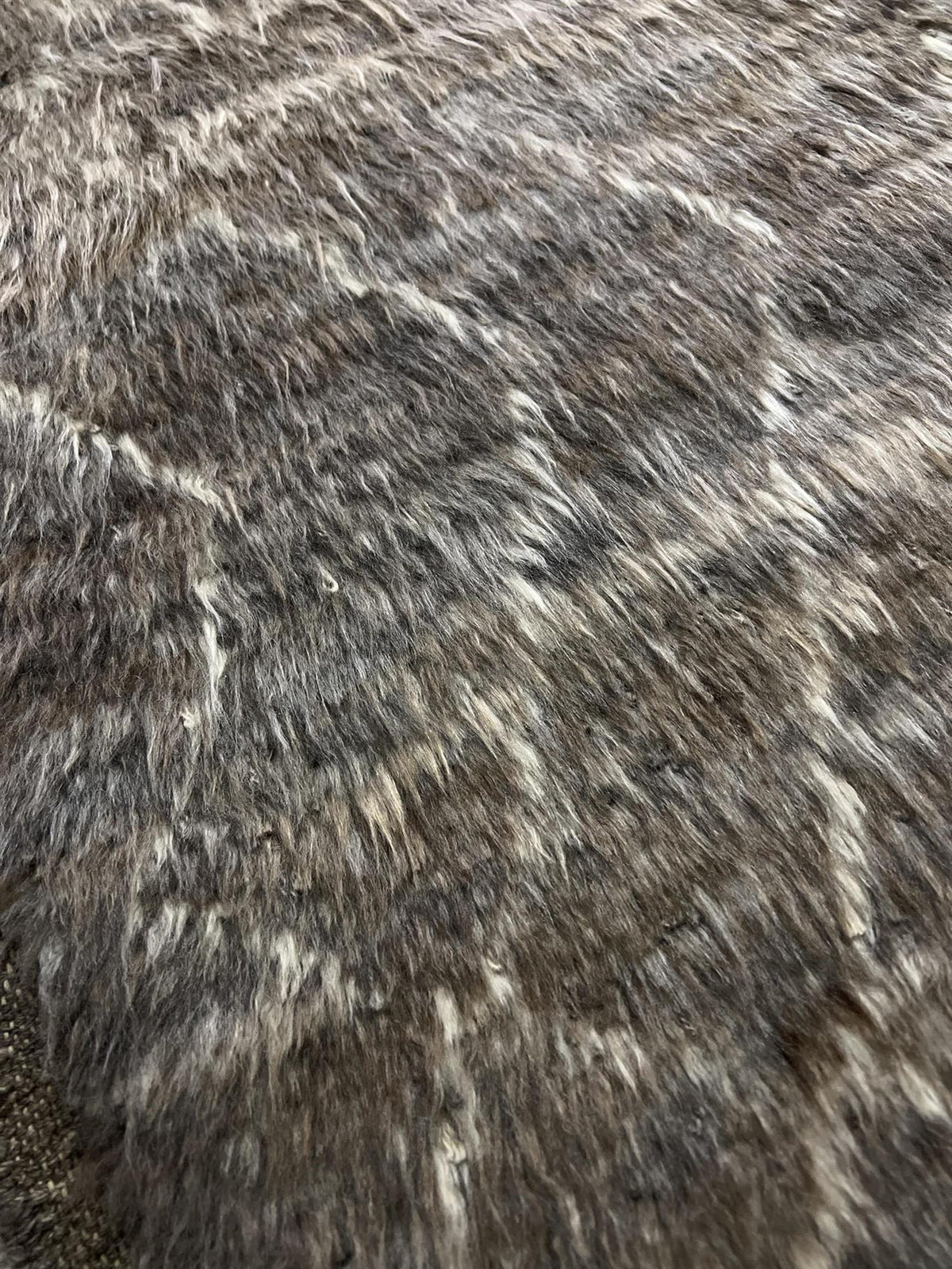A close-up texture shot of a shaggy faux fur or cowhide material in a mottled gray, brown, and white pattern. Atlantica Organics curates antique and handmade rugs, Persian, Afghan, Tibetan, Pakistani, Turkish Oushak, Kilim, Khotan, tribal and contemporary textiles for luxury interiors, homes and real estate. Our collections connect timeless craftsmanship with interior design, furniture, fine art, architecture and modern living. Explore curated rugs, collectible textiles, natural materials, cultural heritage