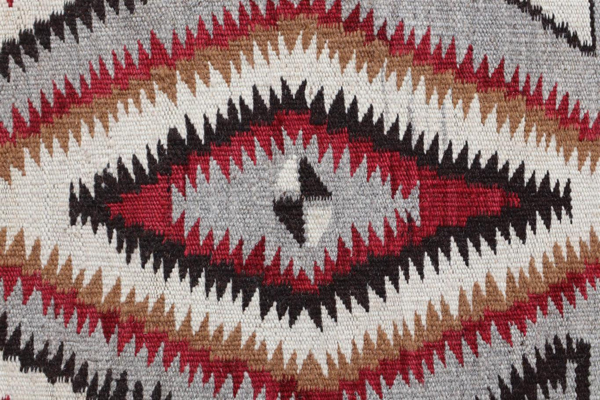 Close-up of a woven textile with a geometric diamond pattern in red, black, tan, and off-white.