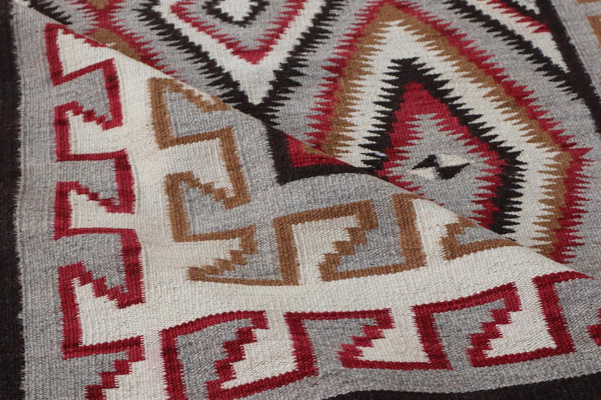Close-up of a woven geometric textile with Southwestern-style patterns in red, brown, black, gray, and off-white.