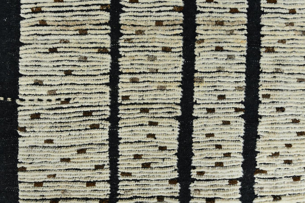 Close-up of a textured woven rug with vertical black stripes and cream sections featuring small brown dotted patterns. Atlantica Organics curates antique and handmade rugs, Persian, Afghan, Tibetan, Pakistani, Turkish Oushak, Kilim, Khotan, tribal and contemporary textiles for luxury interiors, homes and real estate. Our collections connect timeless craftsmanship with interior design, furniture, fine art, architecture and modern living. Explore curated rugs, collectible textiles, natural materials, cultural