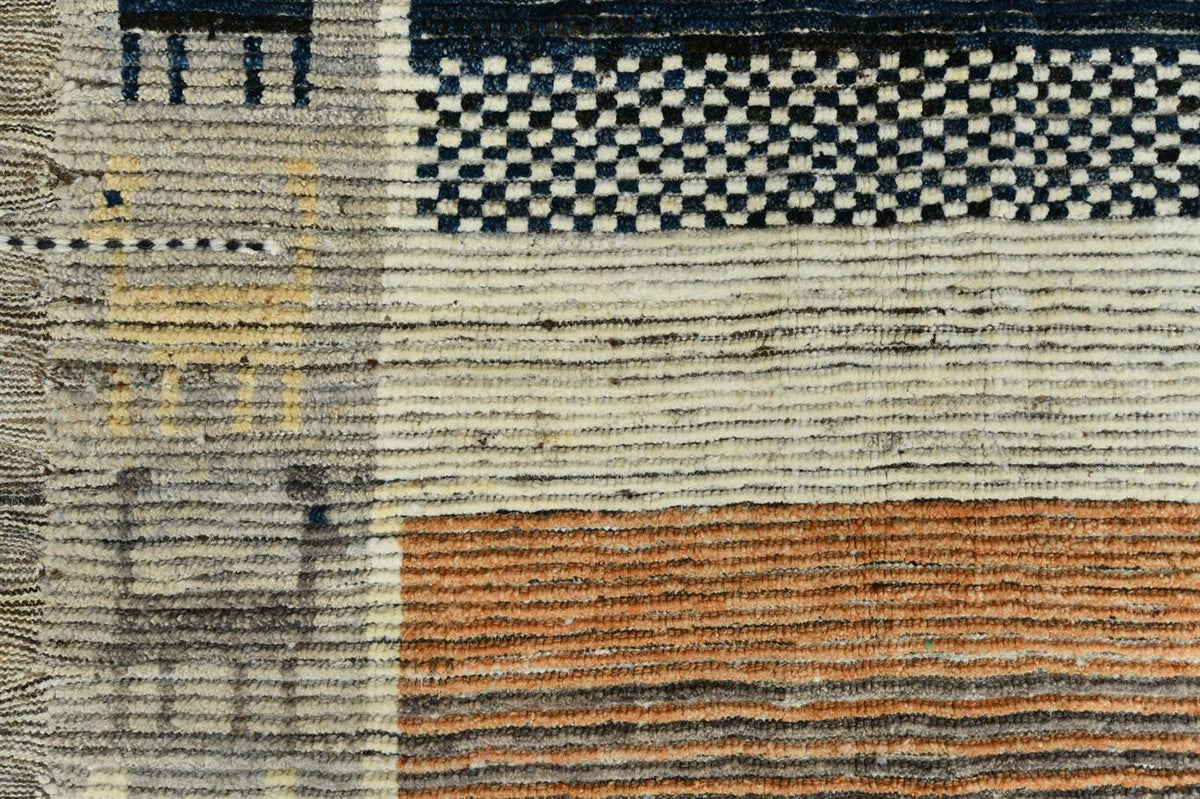 Close-up of a woven rug or textile showing a geometric pattern with cream, navy blue, rust orange, and gray stripes and blocks. Atlantica Organics curates antique and handmade rugs, Persian, Afghan, Tibetan, Pakistani, Turkish Oushak, Kilim, Khotan, tribal and contemporary textiles for luxury interiors, homes and real estate. Our collections connect timeless craftsmanship with interior design, furniture, fine art, architecture and modern living. Explore curated rugs, collectible textiles, natural materials,