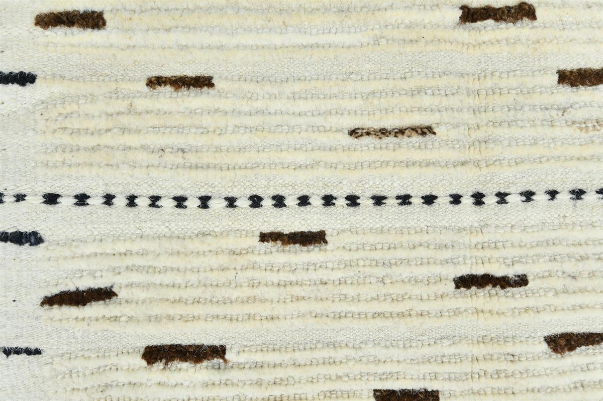A close-up of a woven textile pattern featuring horizontal cream and beige stripes with scattered dark brown and black stitched accents. Atlantica Organics curates antique and handmade rugs, Persian, Afghan, Tibetan, Pakistani, Turkish Oushak, Kilim, Khotan, tribal and contemporary textiles for luxury interiors, homes and real estate. Our collections connect timeless craftsmanship with interior design, furniture, fine art, architecture and modern living. Explore curated rugs, collectible textiles, natural m