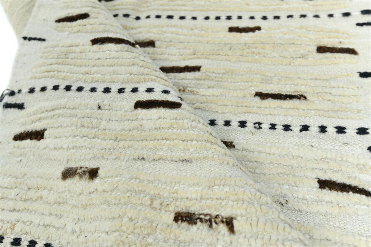A close-up of a textured woven textile, likely a rug or throw blanket, in cream with dark brown and black geometric patterns. Atlantica Organics curates antique and handmade rugs, Persian, Afghan, Tibetan, Pakistani, Turkish Oushak, Kilim, Khotan, tribal and contemporary textiles for luxury interiors, homes and real estate. Our collections connect timeless craftsmanship with interior design, furniture, fine art, architecture and modern living. Explore curated rugs, collectible textiles, natural materials, c
