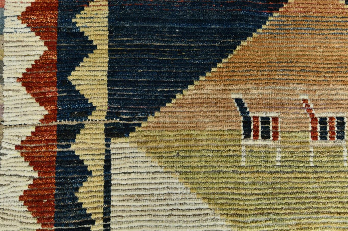 Close-up of a woven rug with a geometric pattern in navy blue, beige, rust red, and muted green, featuring stylized animal motifs on the right side. Atlantica Organics curates antique and handmade rugs, Persian, Afghan, Tibetan, Pakistani, Turkish Oushak, Kilim, Khotan, tribal and contemporary textiles for luxury interiors, homes and real estate. Our collections connect timeless craftsmanship with interior design, furniture, fine art, architecture and modern living. Explore curated rugs, collectible textile