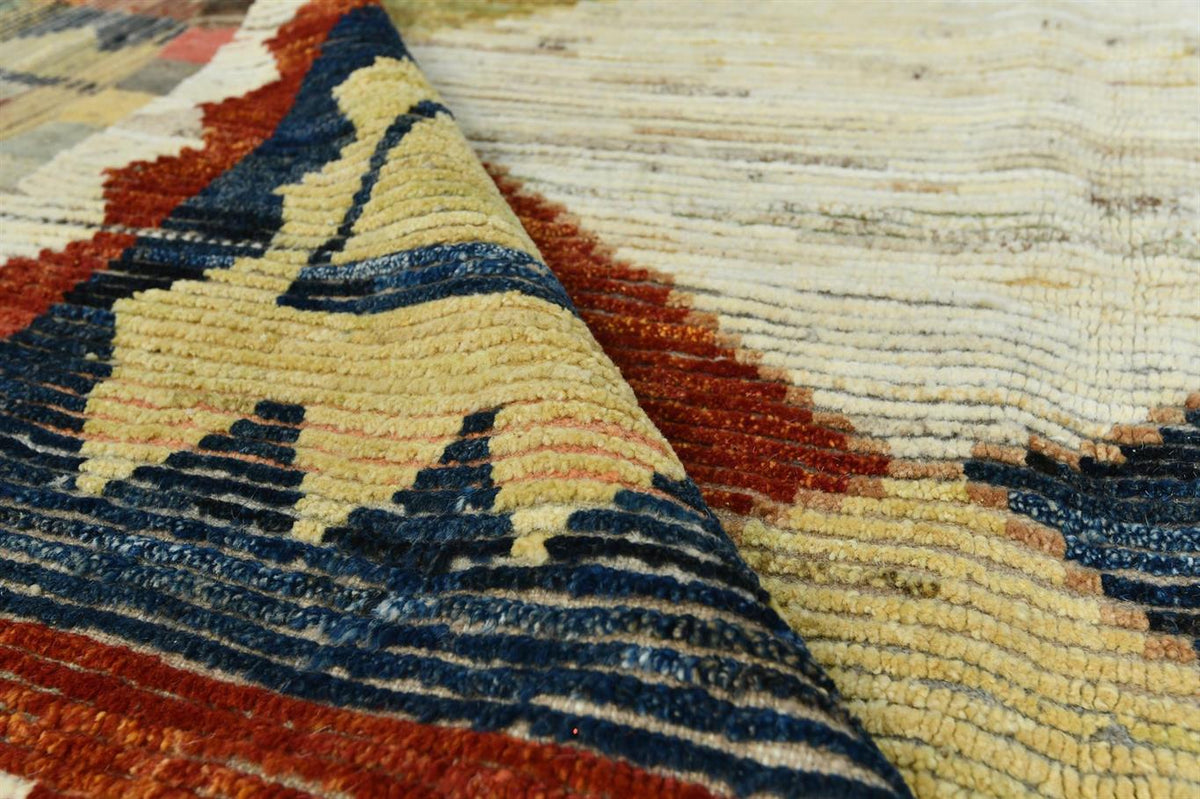 Close-up of a textured area rug with a geometric pattern in cream, navy blue, rust red, and tan, showing the pile texture and folded corner. Atlantica Organics curates antique and handmade rugs, Persian, Afghan, Tibetan, Pakistani, Turkish Oushak, Kilim, Khotan, tribal and contemporary textiles for luxury interiors, homes and real estate. Our collections connect timeless craftsmanship with interior design, furniture, fine art, architecture and modern living. Explore curated rugs, collectible textiles, natur