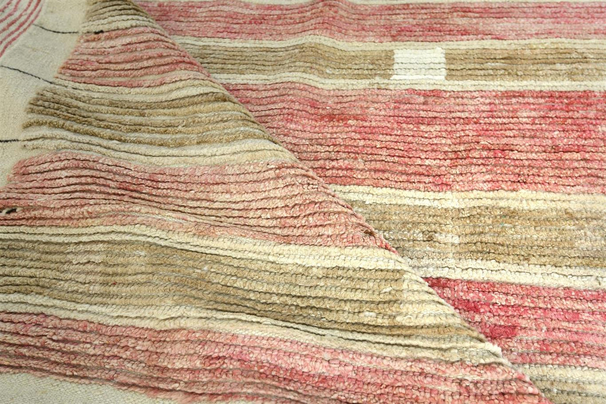 A close-up of a textured woven rug with horizontal stripes in dusty pink, beige, and cream. Atlantica Organics curates antique and handmade rugs, Persian, Afghan, Tibetan, Pakistani, Turkish Oushak, Kilim, Khotan, tribal and contemporary textiles for luxury interiors, homes and real estate. Our collections connect timeless craftsmanship with interior design, furniture, fine art, architecture and modern living. Explore curated rugs, collectible textiles, natural materials, cultural heritage, sustainable desi