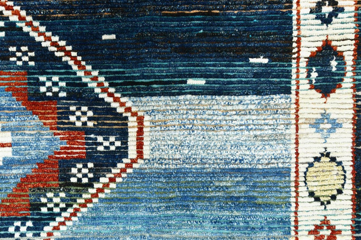 Close-up of a woven rug showing a blue field with geometric tribal patterns in red, cream, black, and white. Atlantica Organics curates antique and handmade rugs, Persian, Afghan, Tibetan, Pakistani, Turkish Oushak, Kilim, Khotan, tribal and contemporary textiles for luxury interiors, homes and real estate. Our collections connect timeless craftsmanship with interior design, furniture, fine art, architecture and modern living. Explore curated rugs, collectible textiles, natural materials, cultural heritage,
