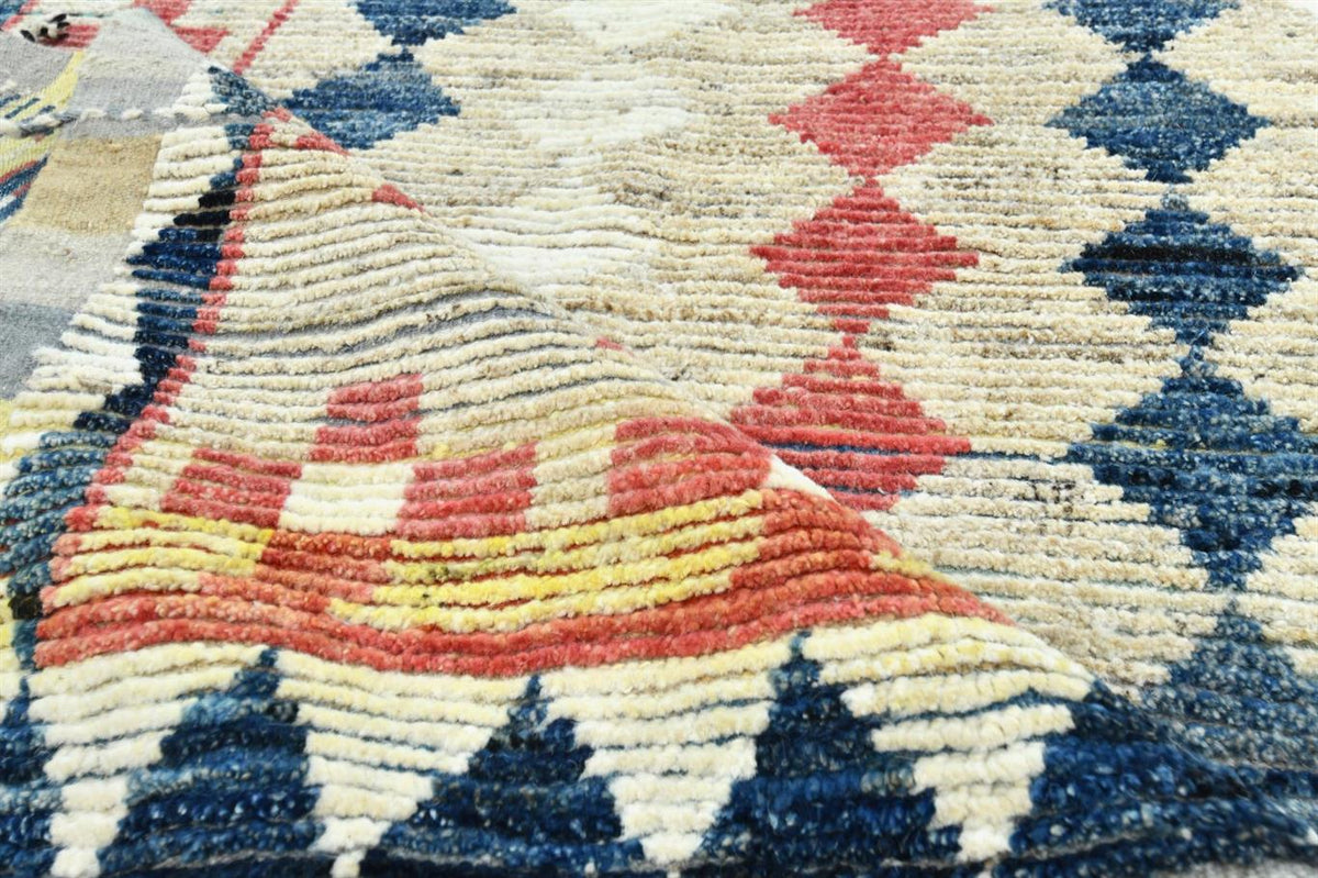 A close-up of a textured, hand-woven Moroccan rug featuring geometric patterns in navy blue, red, yellow, and cream. Atlantica Organics curates antique and handmade rugs, Persian, Afghan, Tibetan, Pakistani, Turkish Oushak, Kilim, Khotan, tribal and contemporary textiles for luxury interiors, homes and real estate. Our collections connect timeless craftsmanship with interior design, furniture, fine art, architecture and modern living. Explore curated rugs, collectible textiles, natural materials, cultural h