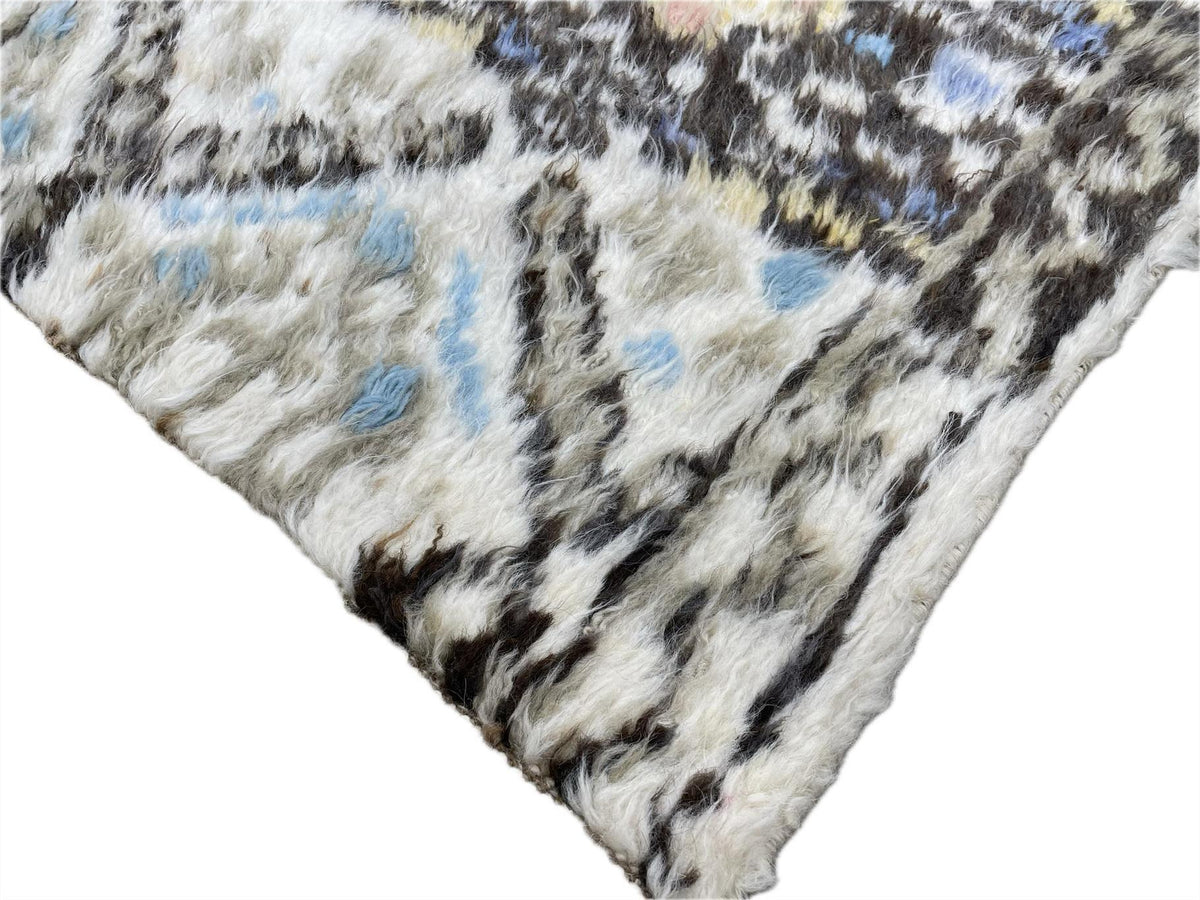 A close-up of a shaggy faux fur textile with an abstract pattern in off-white, black, gray, and light blue, shown against a plain white background. Atlantica Organics curates antique and handmade rugs, Persian, Afghan, Tibetan, Pakistani, Turkish Oushak, Kilim, Khotan, tribal and contemporary textiles for luxury interiors, homes and real estate. Our collections connect timeless craftsmanship with interior design, furniture, fine art, architecture and modern living. Explore curated rugs, collectible textiles