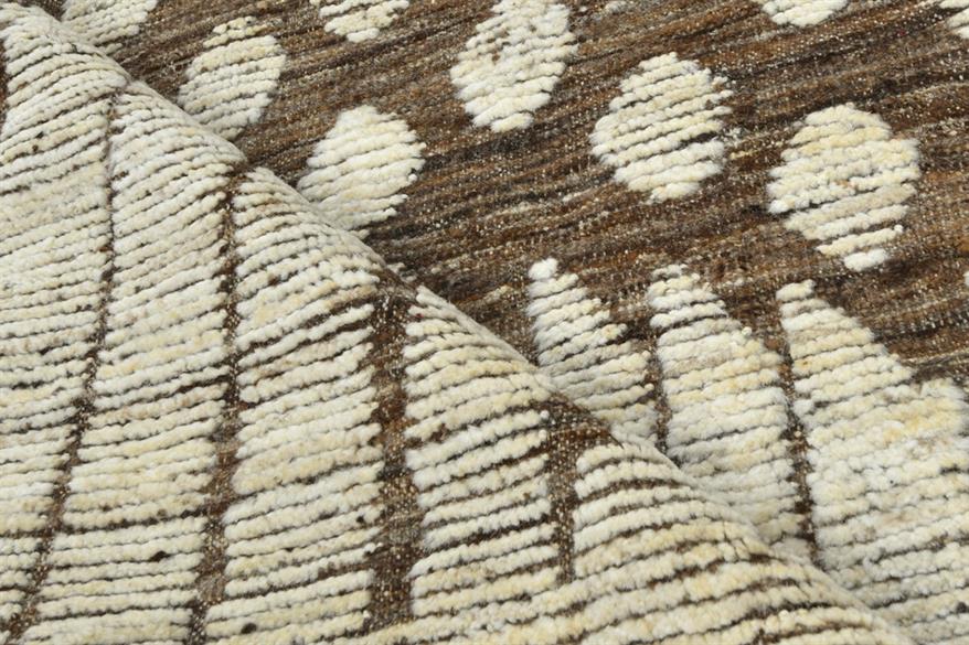 Close-up of a woven textile with a brown and cream geometric pattern, showing the texture and fold of the fabric. Atlantica Organics curates antique and handmade rugs, Persian, Afghan, Tibetan, Pakistani, Turkish Oushak, Kilim, Khotan, tribal and contemporary textiles for luxury interiors, homes and real estate. Our collections connect timeless craftsmanship with interior design, furniture, fine art, architecture and modern living. Explore curated rugs, collectible textiles, natural materials, cultural heri