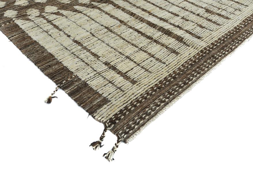 A close-up of a woven rug corner showing a cream and dark brown striped pattern with fringed tassels on a white background. Atlantica Organics curates antique and handmade rugs, Persian, Afghan, Tibetan, Pakistani, Turkish Oushak, Kilim, Khotan, tribal and contemporary textiles for luxury interiors, homes and real estate. Our collections connect timeless craftsmanship with interior design, furniture, fine art, architecture and modern living. Explore curated rugs, collectible textiles, natural materials, cul