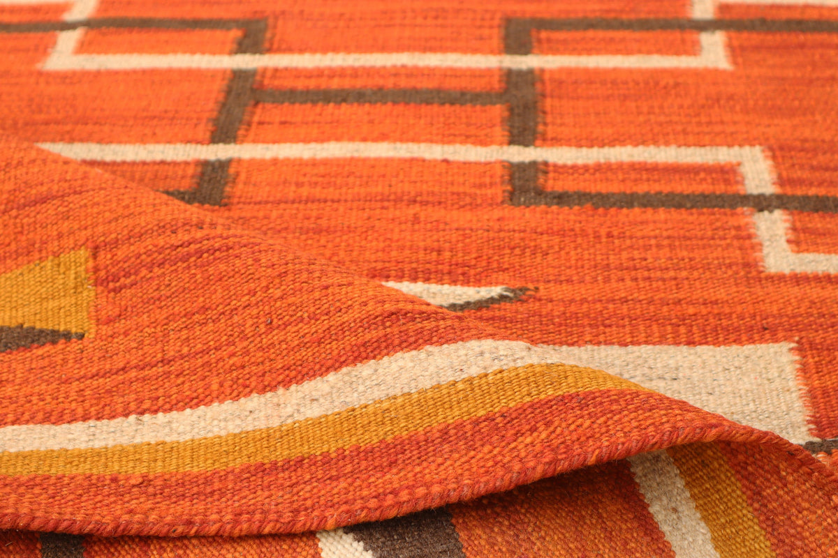 Close-up of a woven textile with an orange base and geometric pattern in cream, mustard yellow, and dark brown.Atlantica Organics curates antique and handmade rugs, Persian, Afghan, Tibetan, Pakistani, Turkish Oushak, Kilim, Khotan, tribal and contemporary textiles for luxury interiors, homes and real estate. Our collections connect timeless craftsmanship with interior design, furniture, fine art, architecture and modern living. Explore curated rugs, collectible textiles, natural materials, cultural heritag