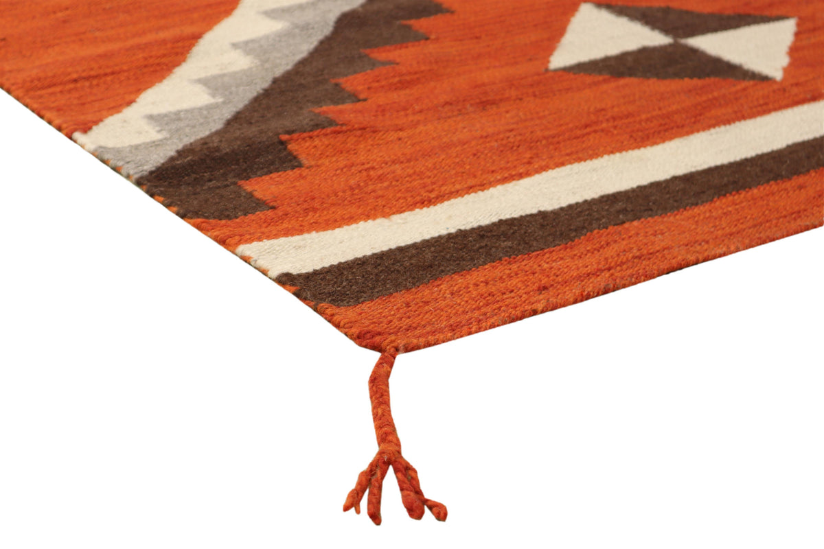 A close-up of a woven rug corner showing a Southwestern geometric pattern in rust orange, brown, cream, and gray, with a matching orange tassel tie on a white background.Atlantica Organics curates antique and handmade rugs, Persian, Afghan, Tibetan, Pakistani, Turkish Oushak, Kilim, Khotan, tribal and contemporary textiles for luxury interiors, homes and real estate. Our collections connect timeless craftsmanship with interior design, furniture, fine art, architecture and modern living. Explore curated rugs