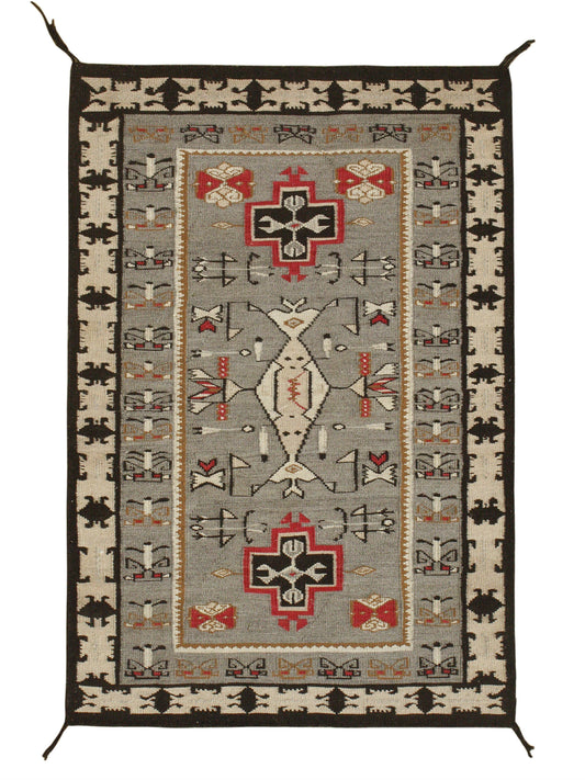 A rectangular woven rug with a Southwestern geometric pattern, featuring a central gray field, beige borders, and red, black, and white motifs. Atlantica Organics curates antique and handmade rugs, Persian, Afghan, Tibetan, Pakistani, Turkish Oushak, Kilim, Khotan, tribal and contemporary textiles for luxury interiors, homes and real estate. Our collections connect timeless craftsmanship with interior design, furniture, fine art, architecture and modern living. Explore curated rugs, collectible textiles, na