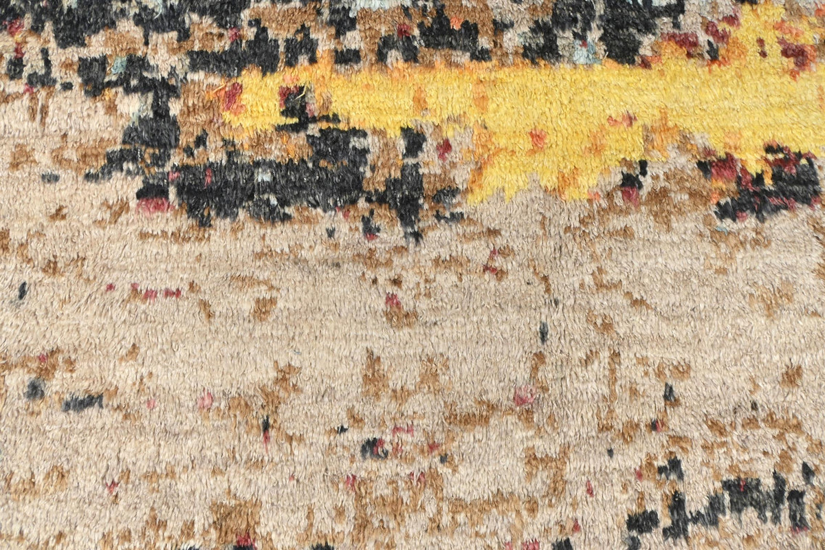 A close-up texture shot of a plush area rug, showing a distressed abstract pattern with a prominent bright yellow band across the top and a mottled beige, brown, and black base. Atlantica Organics curates antique and handmade rugs, Persian, Afghan, Tibetan, Pakistani, Turkish Oushak, Kilim, Khotan, tribal and contemporary textiles for luxury interiors, homes and real estate. Our collections connect timeless craftsmanship with interior design, furniture, fine art, architecture and modern living. Explore cura