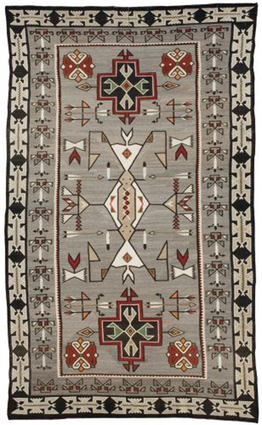 A rectangular Southwestern-style area rug with a geometric pattern, featuring a central field in light gray with red, black, beige, and white motifs, surrounded by a dark border. Atlantica Organics curates antique and handmade rugs, Persian, Afghan, Tibetan, Pakistani, Turkish Oushak, Kilim, Khotan, tribal and contemporary textiles for luxury interiors, homes and real estate. Our collections connect timeless craftsmanship with interior design, furniture, fine art, architecture and modern living. Explore cur