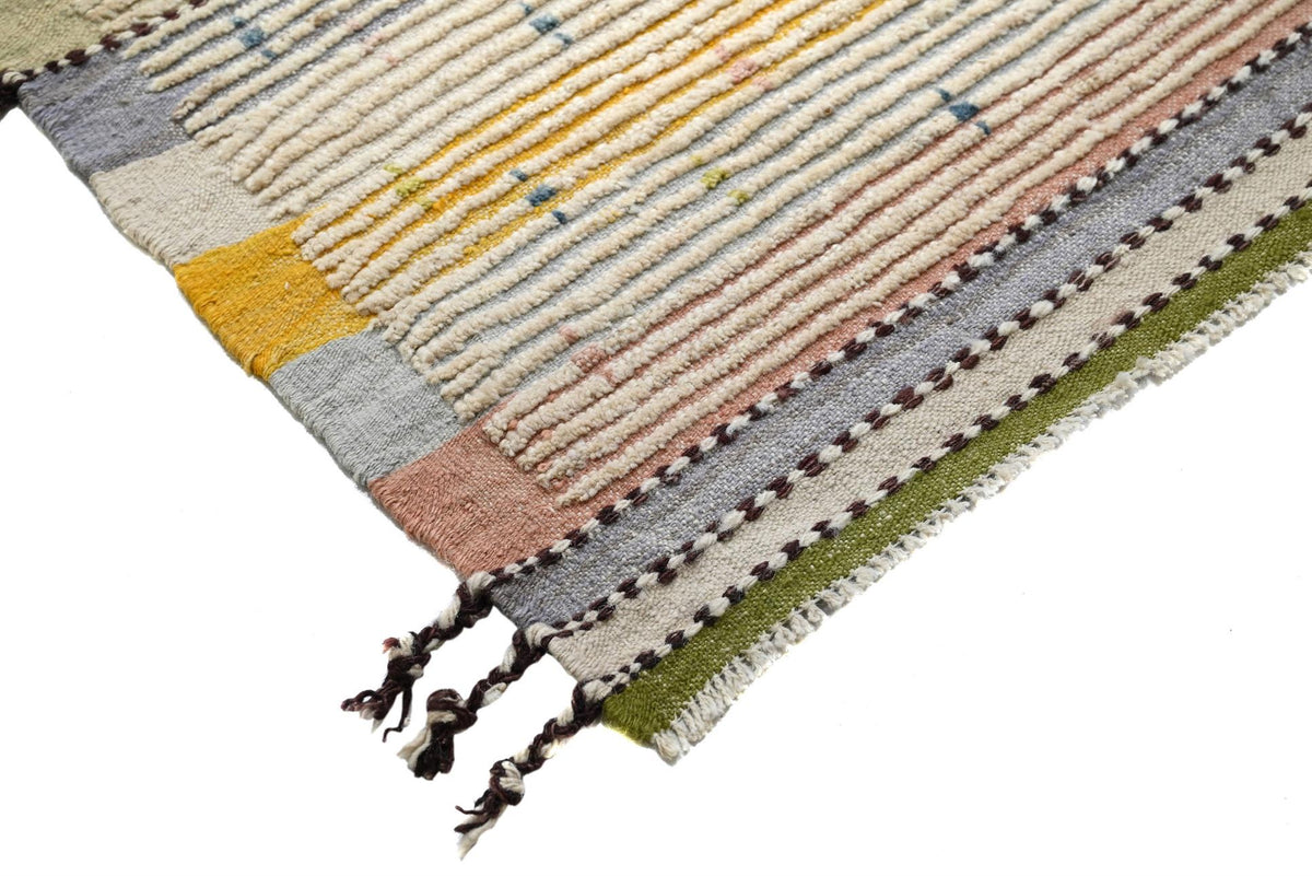 A close-up of a woven rug corner showing striped patterns in beige, yellow, pink, gray, and green with dark tassels on a white background. Atlantica Organics curates antique and handmade rugs, Persian, Afghan, Tibetan, Pakistani, Turkish Oushak, Kilim, Khotan, tribal and contemporary textiles for luxury interiors, homes and real estate. Our collections connect timeless craftsmanship with interior design, furniture, fine art, architecture and modern living. Explore curated rugs, collectible textiles, natural
