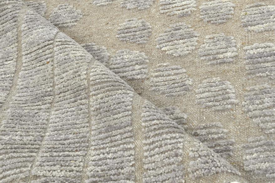 Close-up of a woven textile with a textured geometric pattern in light gray and beige, showing the fabric's ribbed weave and folded corner. Atlantica Organics curates antique and handmade rugs, Persian, Afghan, Tibetan, Pakistani, Turkish Oushak, Kilim, Khotan, tribal and contemporary textiles for luxury interiors, homes and real estate. Our collections connect timeless craftsmanship with interior design, furniture, fine art, architecture and modern living. Explore curated rugs, collectible textiles, natura